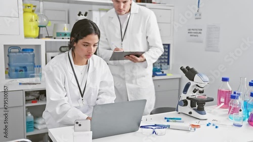 A man and woman in white lab coats working together in a science laboratory filled with research equipment photo