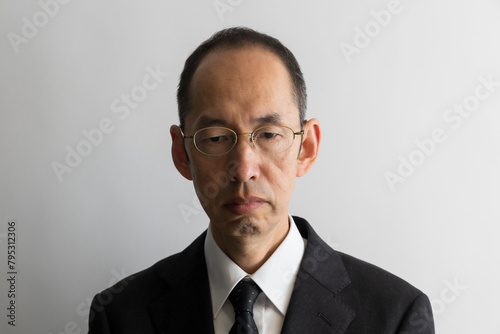 うつむいたメガネをかけたスーツ姿の日本人の中年男性のポートレイト