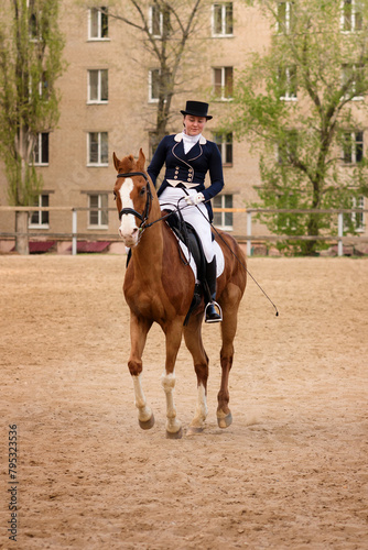 Dressage rider and chestnut horse poised in sandy urban arena
