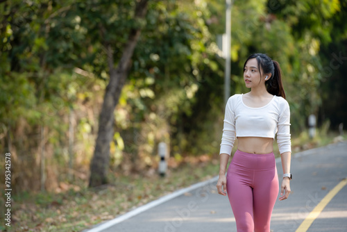 Happy athletic woman with crossed arms wearing a fitness smartwatch on a sunny park pathway. © Wasana