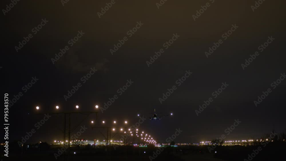 Airplane with landing lights on descending towards the runway with guiding lights visible at night Airplane with landing lights on descending towards the runway with guiding lights visible at night