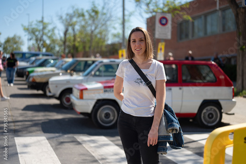 Portrait of a young smiling girl who is fond of the world of motors at a classic car meetup on the street of Barcelona. It's summer and it's a sunny day.