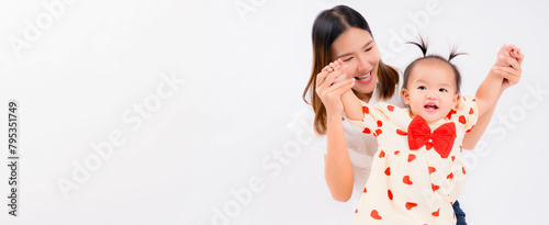 Young Asian mother holding child's hands for practicing her baby stand up and walking A cheerful mother playing with her delighted baby against a white background, both smiling.
