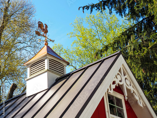 Copper rooster weathervane and cupola on red shed or barn with dark metal roof