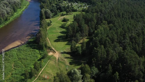 Valmiera, Latvia - August 20, 2023 - Aerial view of a river bending alongside a disc golf course in a forested area, grassy fields, pathways, trees, clear summer day. photo