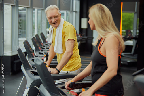 Two cheerful seniors, man and woman in sportwear working out together on gym machines. Concept of sport, active seniors in modern life, healthy lifestyle, fitness. Ad