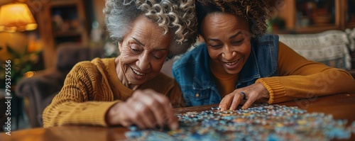 A smiling female caregiver aids a senior woman with a puzzle at home, depicting companionship and assistance. © vadymstock
