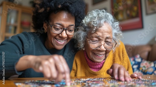 A smiling female caregiver aids a senior woman with a puzzle at home, depicting companionship and assistance.