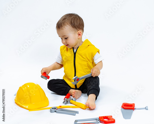 A young child is playing with a toy set that includes a yellow hard hat and a wrench. The child is sitting on the floor and he is enjoying the activity