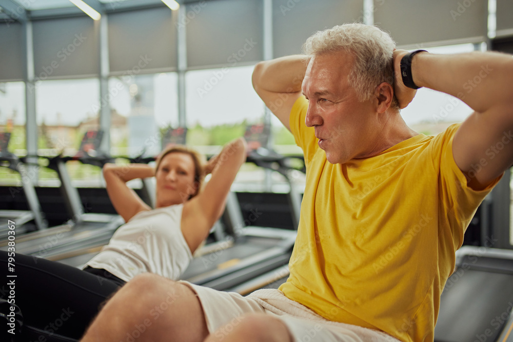 Active mature couple doing abdominal exercises together in modern fitness center, man and woman looks focused. Concept of sport, active seniors in modern life, healthy lifestyle. Ad Active mature couple doing abdominal exercises together in modern fitness center, man and woman looks focused. Concept of sport, active seniors in modern life, healthy lifestyle. Ad