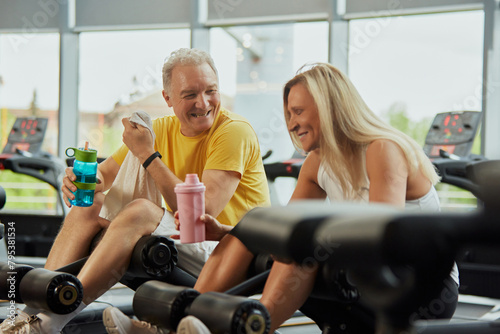 Two seniors in wearing sport gear share fun moment during exercising in modern fitness center. Concept of sport, active seniors in modern life, healthy lifestyle, fitness, strength and vitality. Ad