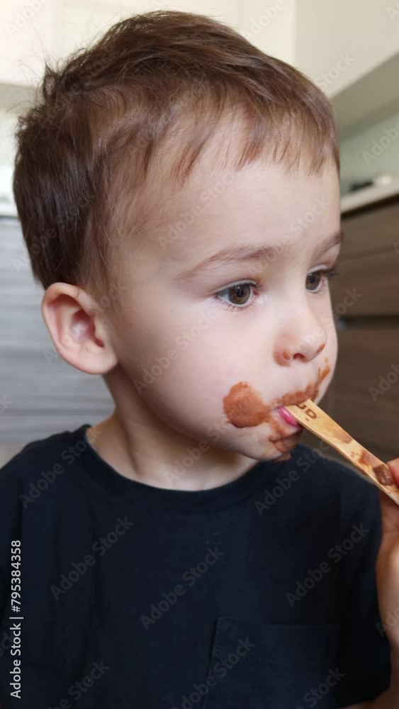 Cute kid with chocolate stains around his mouth licking the stick from ice-cream. Sweet tooth child enjoying the dessert. Close up. Vertical video. Cute kid with chocolate stains around his mouth licking the stick from ice-cream. Sweet tooth child enjoying the dessert. Close up. Vertical video.