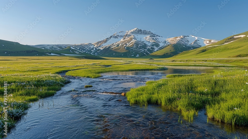 A crystal-clear river meanders through an alpine meadow, with the last traces of melting snow adorning the mountain peaks under a blue sky.