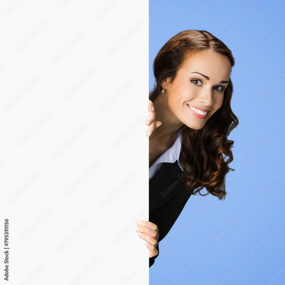 Happy smile woman in black confident suit, peep out hold blank white poster banner signboard with empty sign text. Business ad concept. Isolated against blue background. Square image Happy smile woman in black confident suit, peep out hold blank white poster banner signboard with empty sign text. Business ad concept. Isolated against blue background. Square image