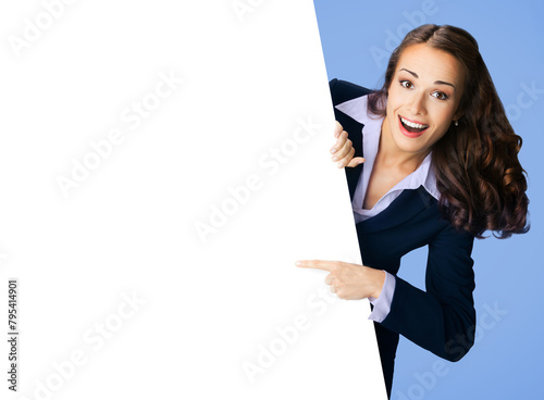 Happy smile woman in black confident suit, peep out show pointing advertise blank white banner signboard poster with empty ad sign text place. Business ad concept. Isolated blue background.