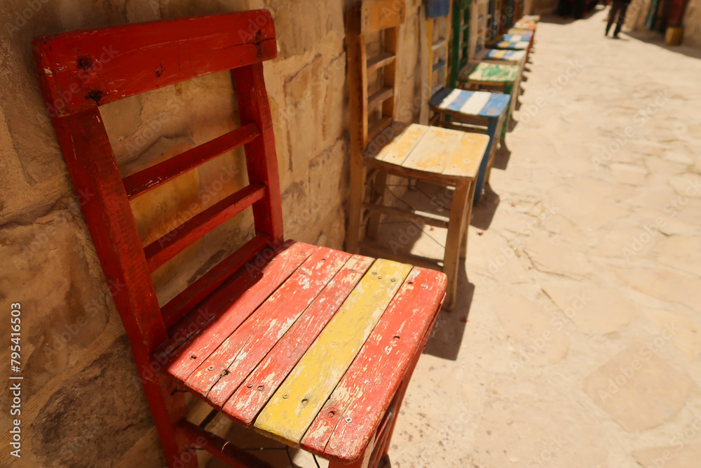 A row of colorful wooden chairs in a row in front of a wall in the old town of Mardin, Turkey