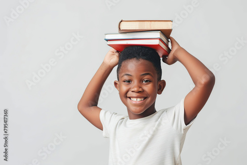 Back to school. Little boy holding a stack of books on his head on beige gray background. Portrait of joyful child after education wants to play. Funny kid balancing book on a head, looking at camera