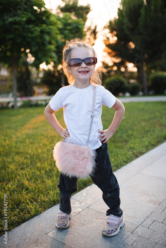 Funny baby girl 4-5 year old wearing casual clothes and sun glasses having fun in park outdoor. Childhood.