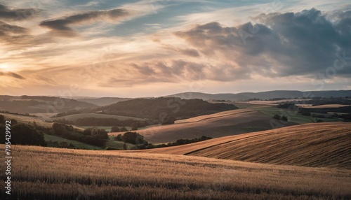 sky with beautiful clouds over rolling hills with stubble field at sunset in summer