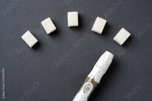 Blood sugar level displayed with sugar cubes and a lancet pen on a dark background © yalcinsonat