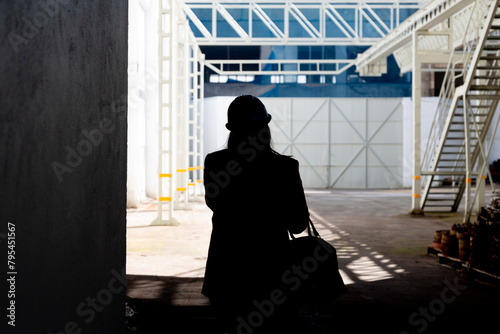 A silhouetted figure stands in a spacious industrial interior, holding a tablet, with beams of light highlighting the surrounding structures