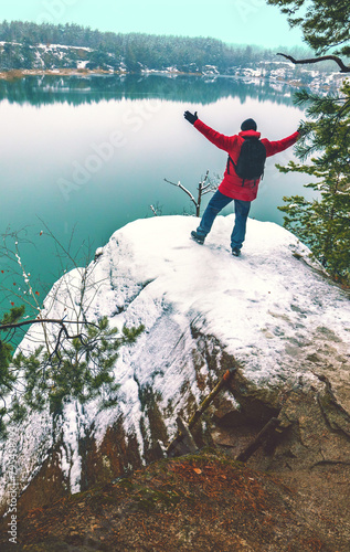 A man with raised hands stands on the snowy shore of a lake in winter and looks at the beautiful view. Vertical image