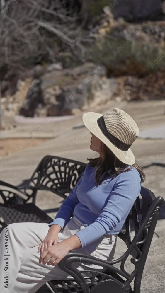 Relaxed woman with hat sitting on park bench in sunny guadalest street landscape Relaxed woman with hat sitting on park bench in sunny guadalest street landscape