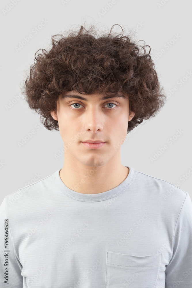 smiling and handsome a young man with curly hair he looks into the camera with his blue eyes, portrait of guy isolated against a gray background smiling and handsome a young man with curly hair he looks into the camera with his blue eyes, portrait of guy isolated against a gray background