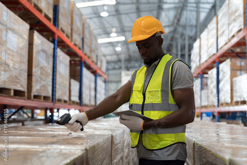 African American male warehouse worker wear safety uniform, helmet and scanning barcodes on boxes in storage warehouse