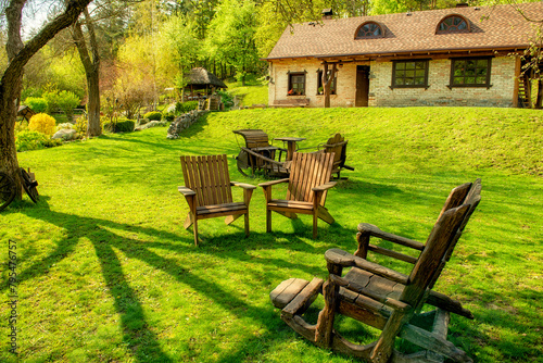 cozy relaxation spot on a green lawn with old wooden chairs near a farmhouse in spring. Ukraine