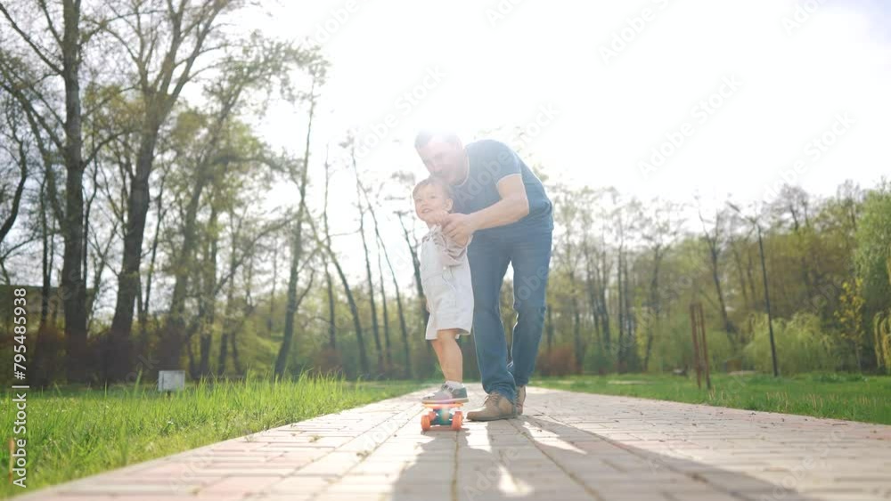 learn to skateboard. dad a teaches his baby toddler son to skateboard in the park. father and son game teaching concept. parent teaching child toddler to ride a skateboard in lifestyle the park