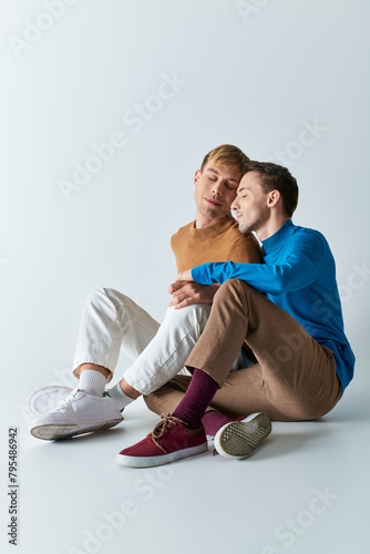 Two men in casual attire sitting on the ground, arms wrapped around each other in a loving embrace.