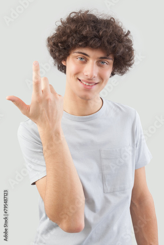 Smiling and handsome a young man with curly hair he looks into the camera with his blue eyes, gesturing with his hands, a portrait of a guy wearing a T-shirt isolated against a gray background