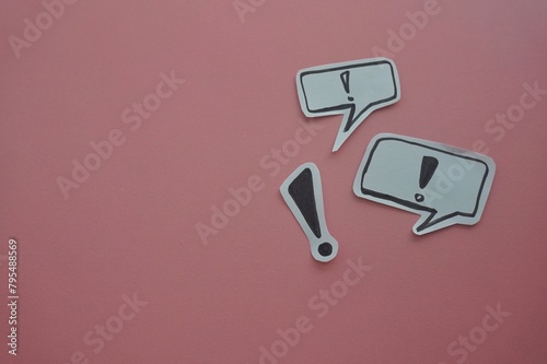 top view of of black exclamation mark on white speech bubble on a pink background.