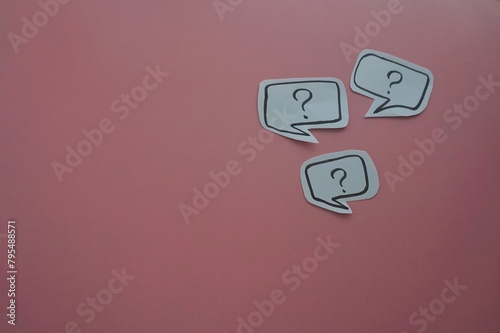 top view of of black question mark on white speech bubble on a pink background.