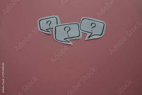 top view of of black question mark on white speech bubble on a pink background.