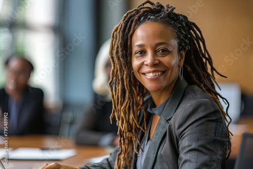 Woman with dreadlocks smiling at the camera during a meeting in a business office. Mature and professional business woman leading a corporate team towards success
 photo