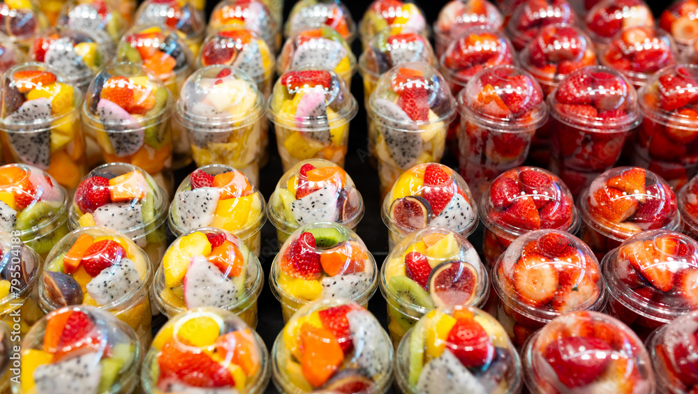 Fruit Salad arranged in plastic cups on a market. Cut and ready fruit ready to sell in market. Convenience, healthy lifestyle. Strawberries, kiwi, melon, pineapple, figs, dragon in a plastic glass.