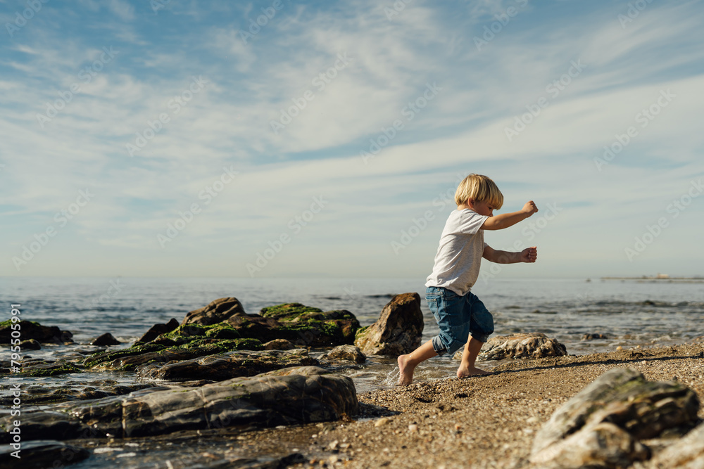 little blond boy playing on the seashore. child playing on the seashore. boy stands on stones in the water. child playing on the seashore little blond boy playing on the seashore. child playing on the seashore. boy stands on stones in the water. child playing on the seashore