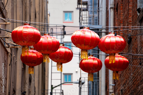 Traditional red chinese lanterns hanging on cables above a city road in Chinatown in downtown San Francisco (California, USA). Rows of shabby electric lamps in a narrow street.