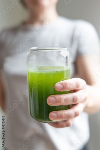 Woman holding glass with drink from young barley and chlorella spirulina powder or matcha tea.