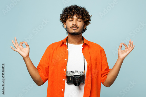 Traveler Indian man in orange casual clothes hold hands in yoga om aum gesture isolated on plain blue background Tourist travel abroad in free spare time rest getaway Air flight trip journey concept #795540724