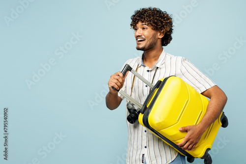 Side view traveler fun smiling Indian man wear white casual clothes hold bag isolated on plain blue background. Tourist travel abroad in free spare time rest getaway. Air flight trip journey concept. #795540902