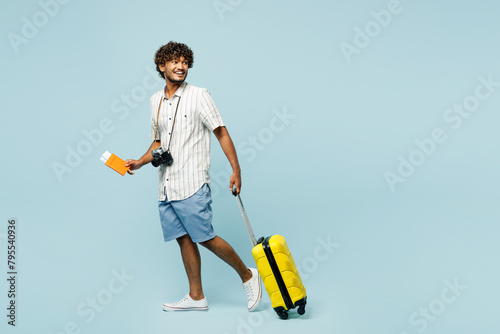 Full body traveler Indian man wear white casual clothes hold bag passport ticket walk isolated on plain blue background Tourist travel abroad in free time rest getaway Air flight trip journey concept