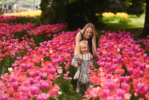 A beautiful little girl walks in a field of tulips. Mom and daughter in a field with flowers. Mom hugs her little daughter. Mother's day mom and daughter