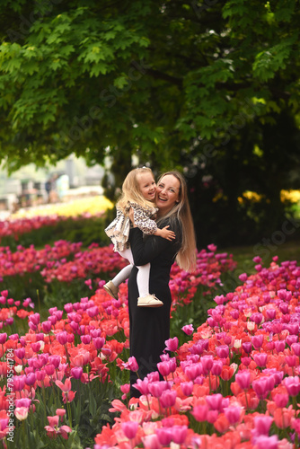A beautiful little girl walks in a field of tulips. Mom and daughter in a field with flowers. Mom hugs her little daughter. Mother's day mom and daughter