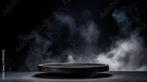 Empty podium for products made of black round polished stone on black background with clouds of smoke and fog. For advertising. Soft illumination of light breaking through fog. Copy space.