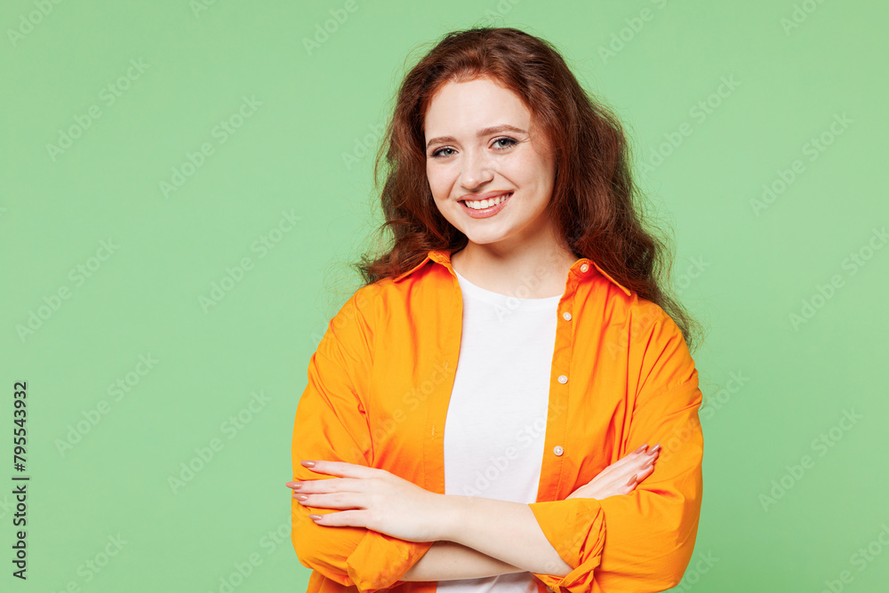 Fototapeta premium Young smiling happy cheerful ginger woman she wearing orange shirt white t-shirt casual clothes hold hands crossed folded look camera isolated on plain pastel light green background Lifestyle concept