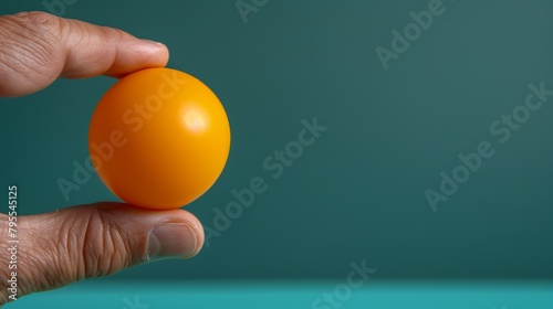  Person's hand holding an orange against a teal green backdrop Single orange in foreground