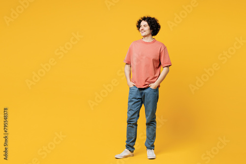 Full body young smiling cheerful happy man he wear pink t-shirt casual clothes hold hands in pockets look aside on area isolated on plain yellow orange background studio portrait. Lifestyle concept.